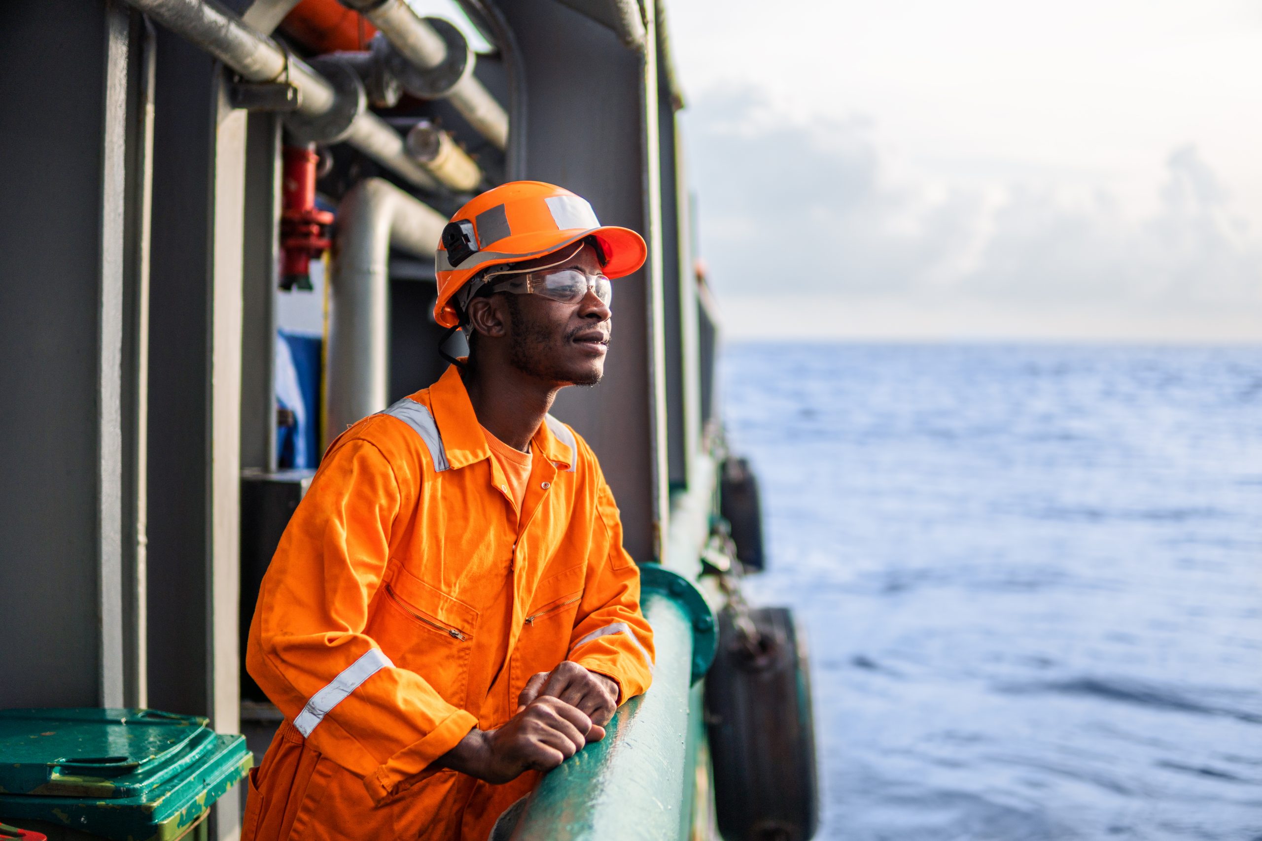 Tired Seaman AB or Bosun on deck of vessel or ship , wearing PPE personal protective equipment - helmet, coverall, lifejacket, goggles. Safety at sea